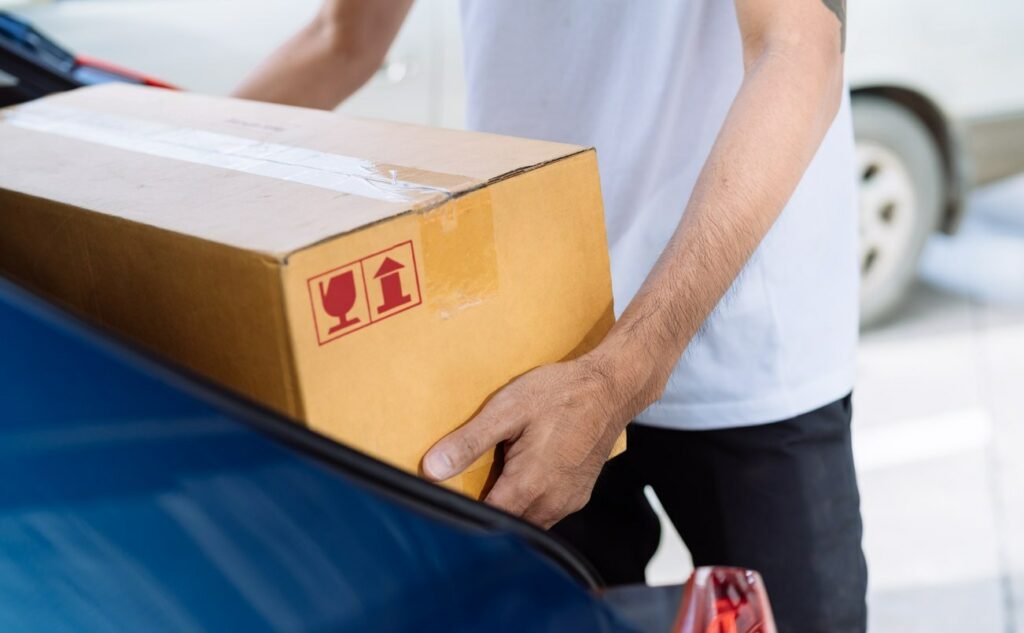 A man removes a cardboard box from the trunk of a blue car.