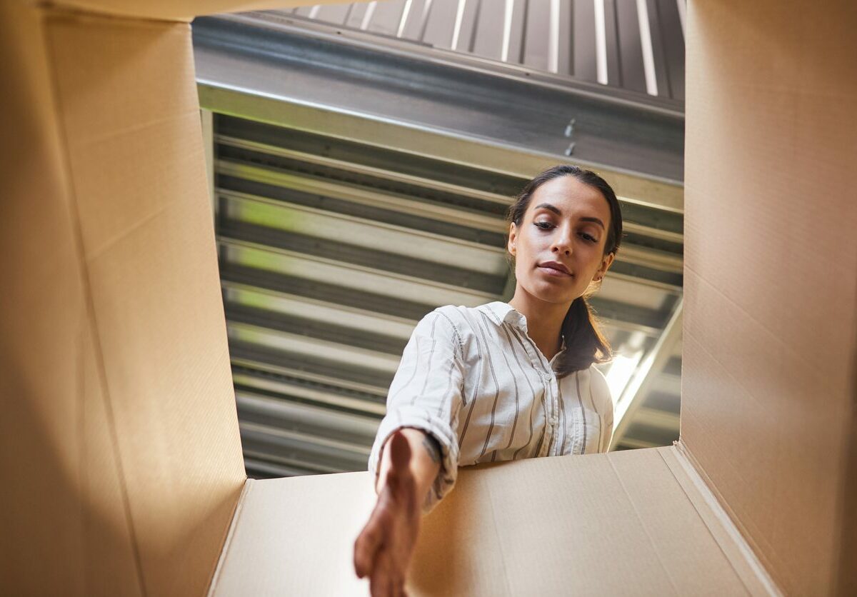 A woman looks down and reaches into a cardboard storage box.
