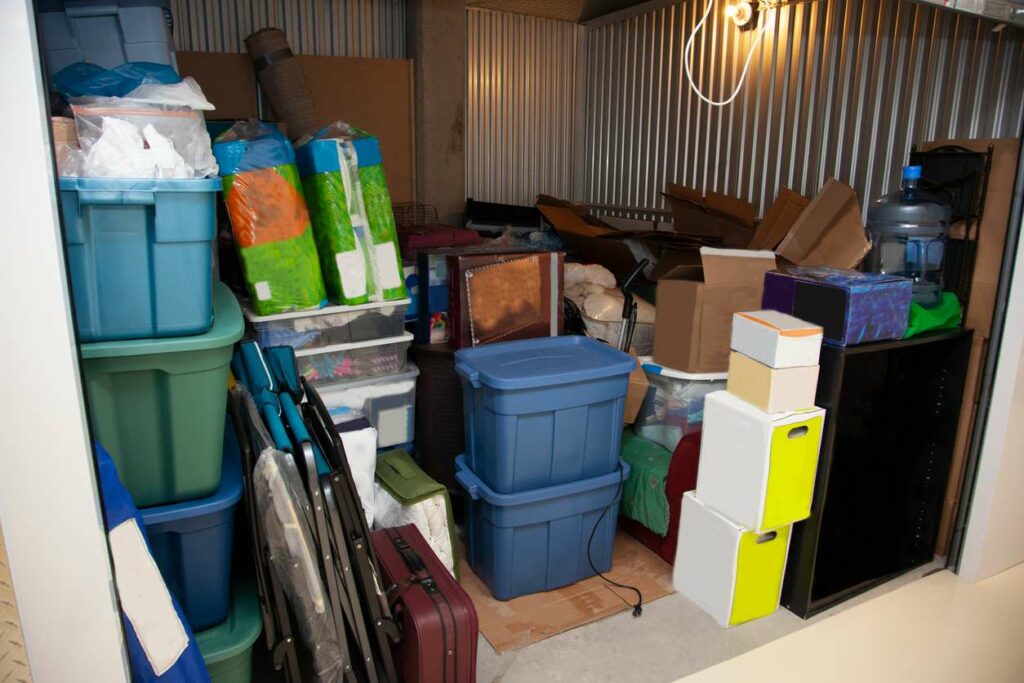 A storage unit is filled with an assortment of tubs, boxes, furniture, and other items