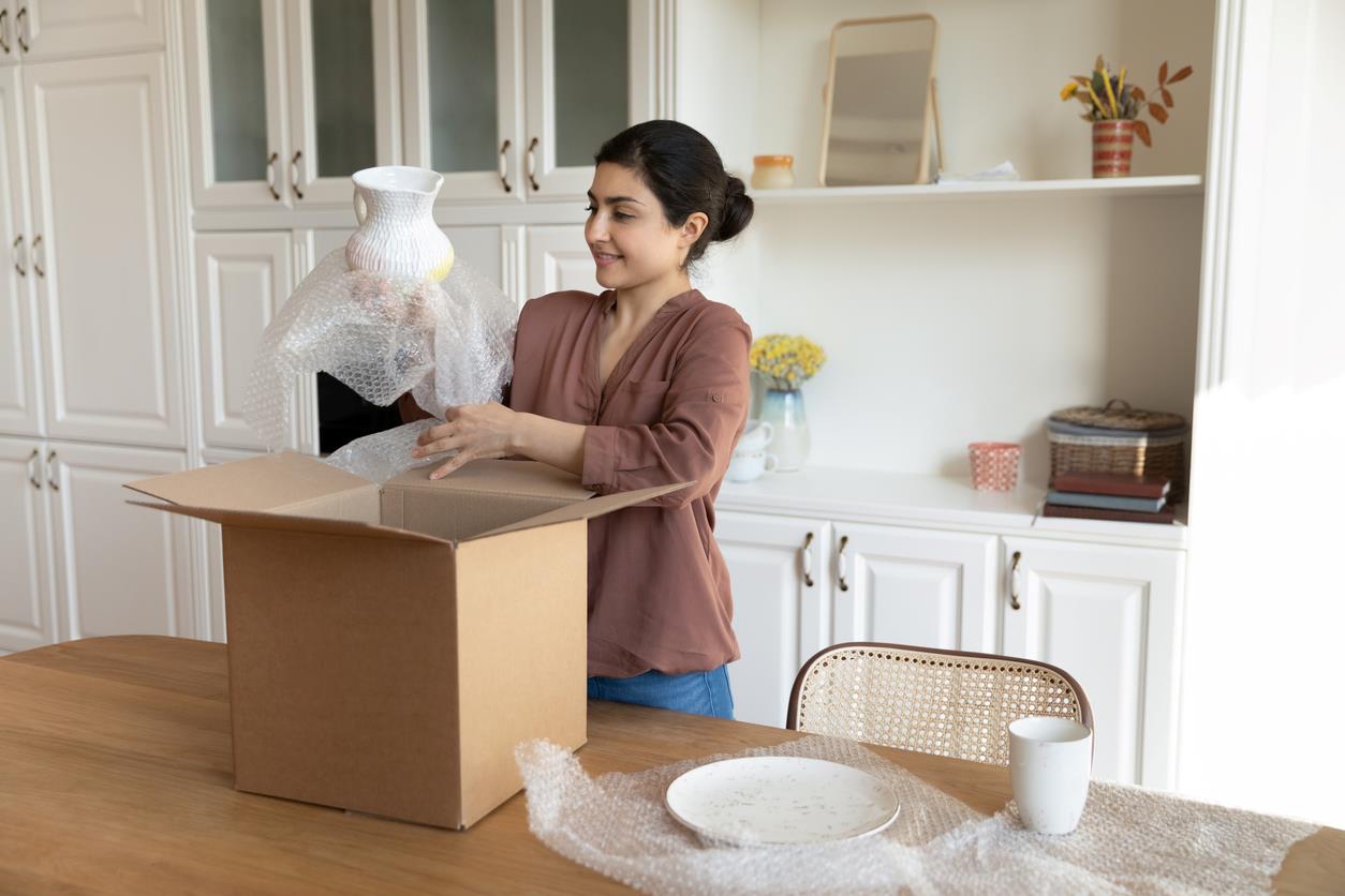 Woman putting dishes wrapped in bubble wrap in a box.