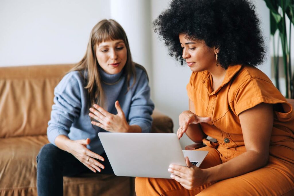 Two stylish women talking while looking at a computer