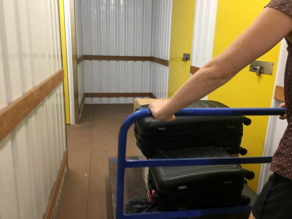 A person pushing their dolly with storage items through a storage facility hallway