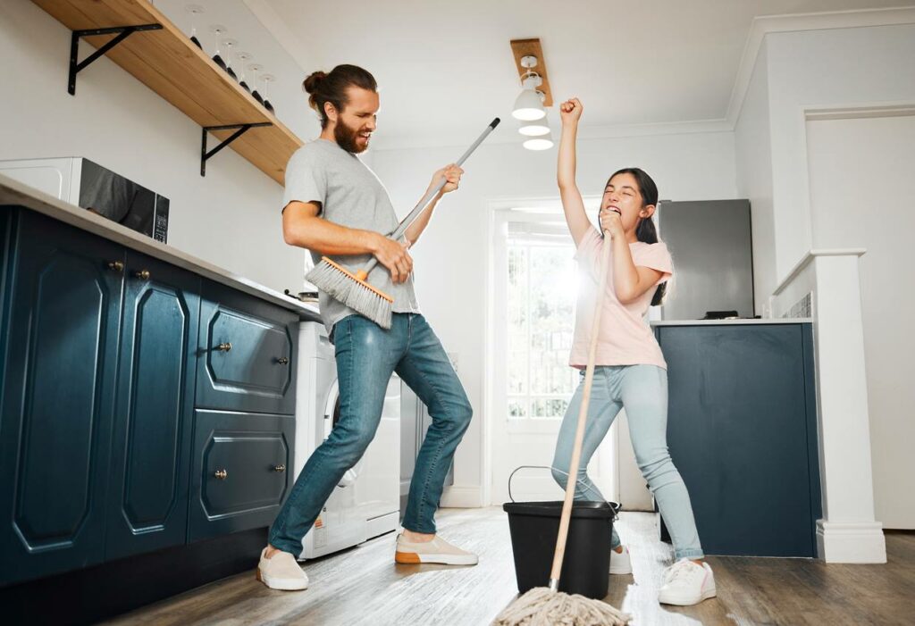 A father and daughter joyfully clean the floor while dancing.