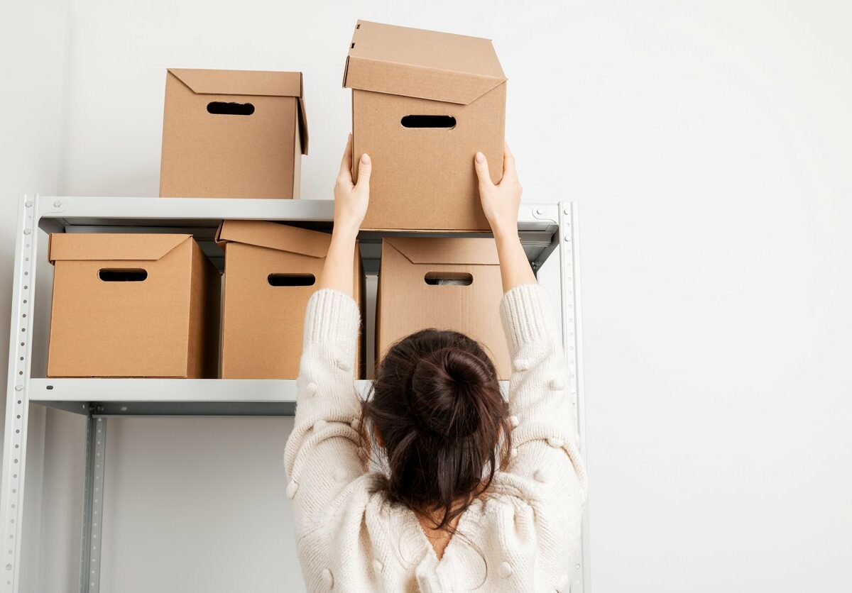 A woman places another cardboard box onto a metal shelf in her storage unit.