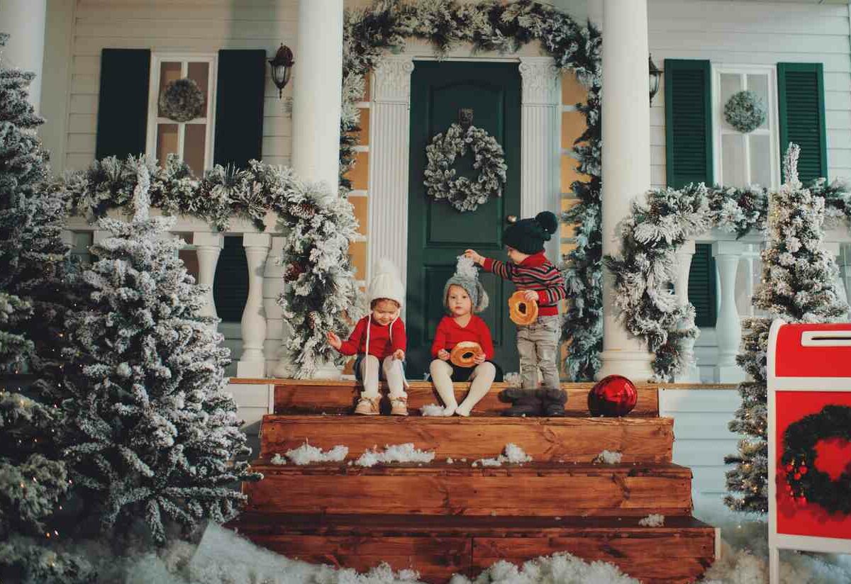 : A Portrait of three children on a decorated winter porch eating a snack.