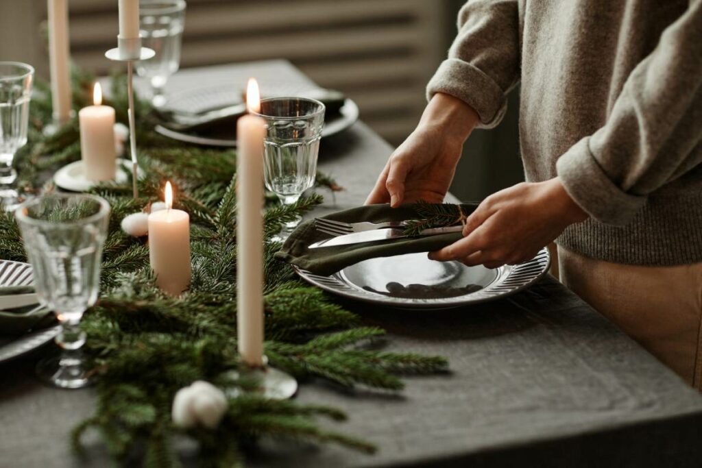 : Close-up of a wintry decorated table with a person setting silverware and napkins on a plate. 