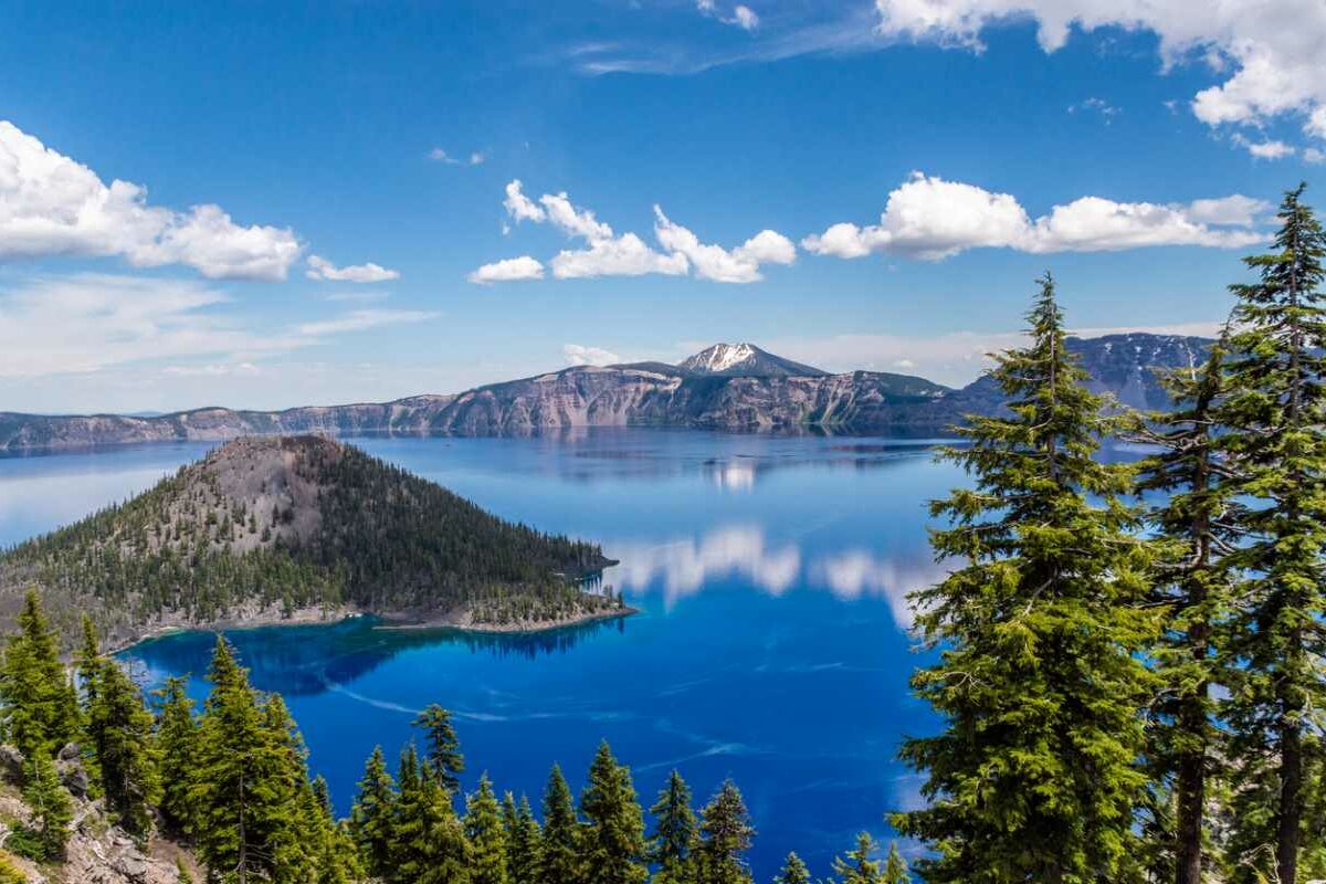 Crater Lake, OR, with blue water, clouds in the sky, and trees.