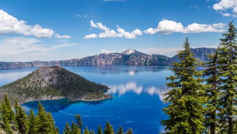 Crater Lake, OR, with blue water, clouds in the sky, and trees.