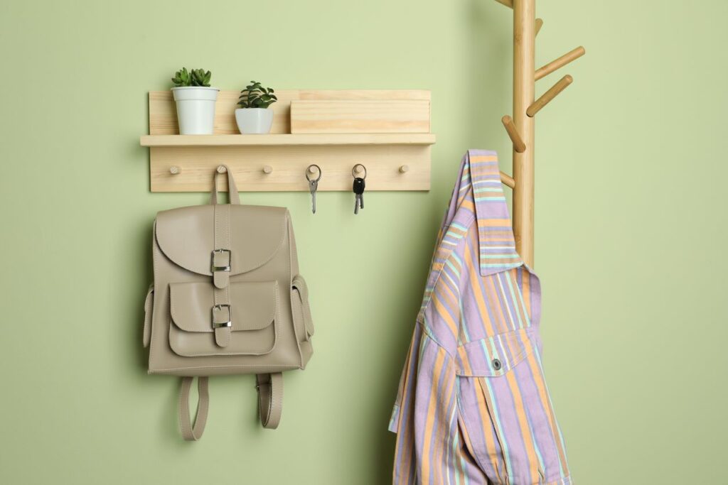 A wooden storage hanger and shelf holds keys, a backpack, and plants in the entryway of a student dorm.