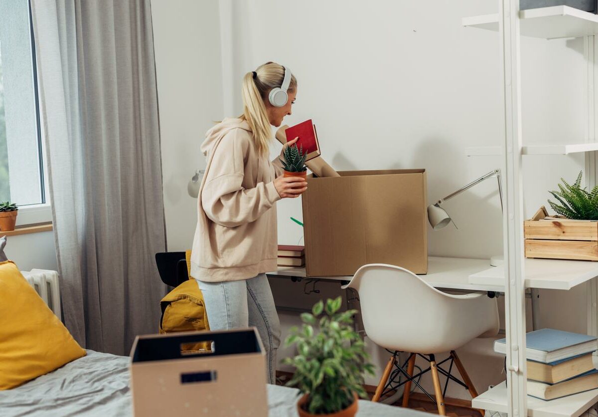 A college student is packing her dorm room into boxes with headphones on.